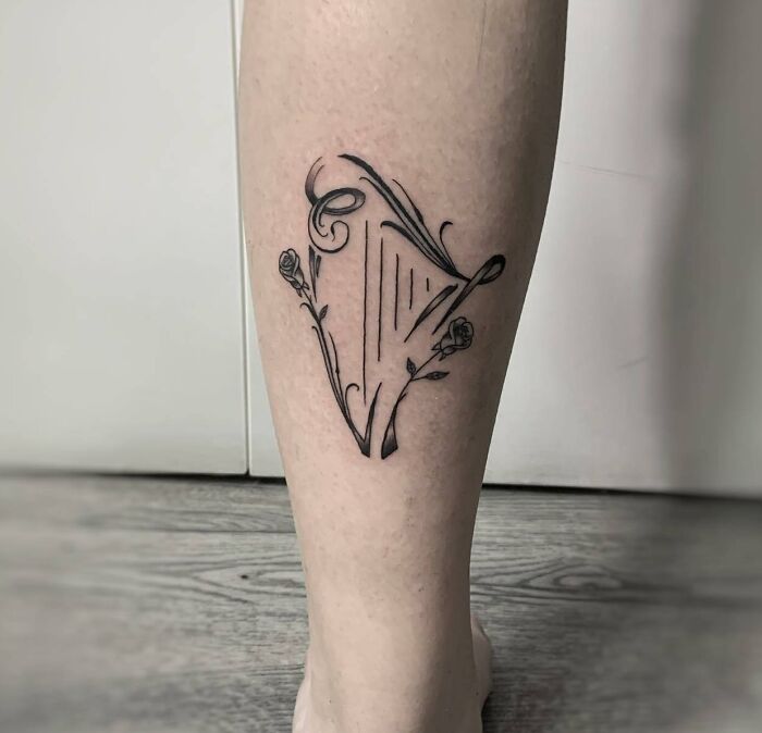 Black minimal floral harp tattoo on leg