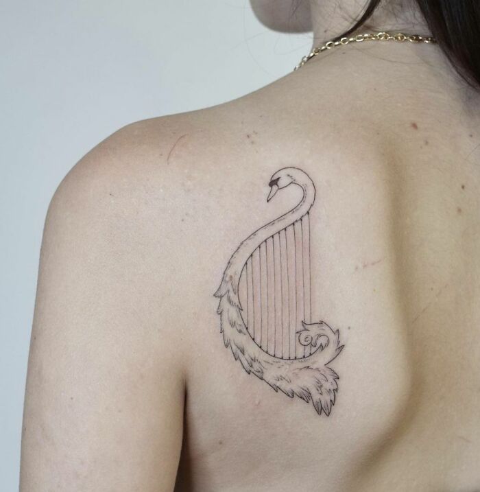 Swan and harp tattoo on a shoulder blade