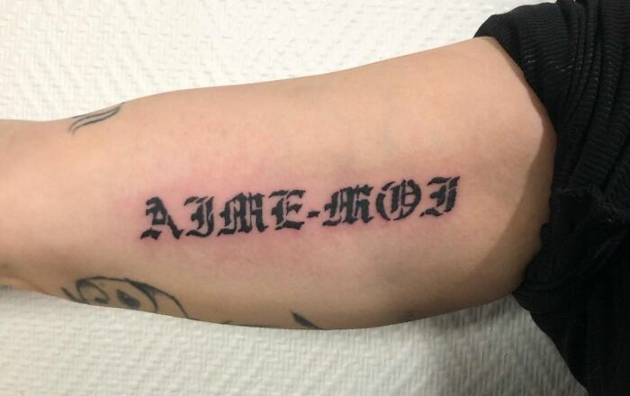 "Aime-moi" dark lettering tattoo on the inside of the arm