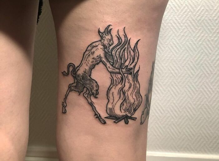 Gothic tattoo depicting a whimsical creature interacting with a stylized fire on skin.