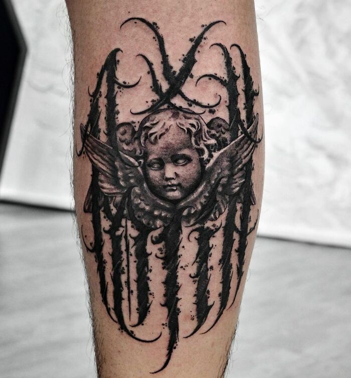 Gothic tattoo of an angel with intricate dark designs on a leg.