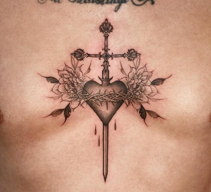 Gothic tattoo of heart pierced by a cross with floral details and barbed wire on chest.
