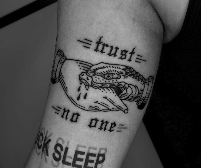 "trust no one" gothic lettering and an etched handshape upper arm tattoo