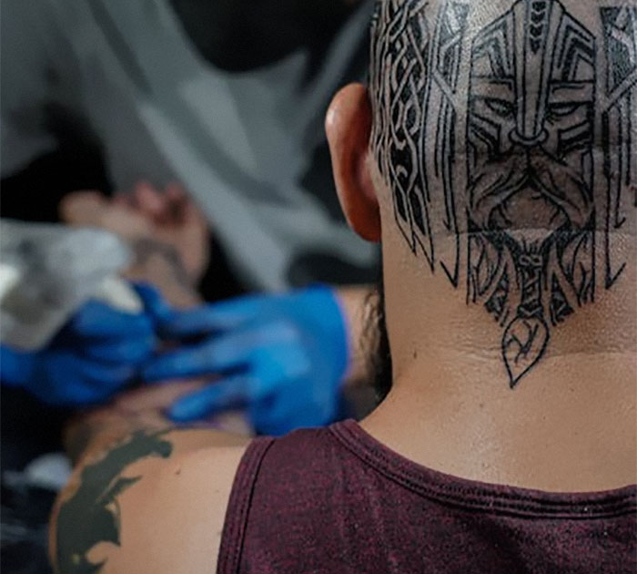 Head tattoo design featuring intricate patterns being inked by an artist wearing blue gloves.