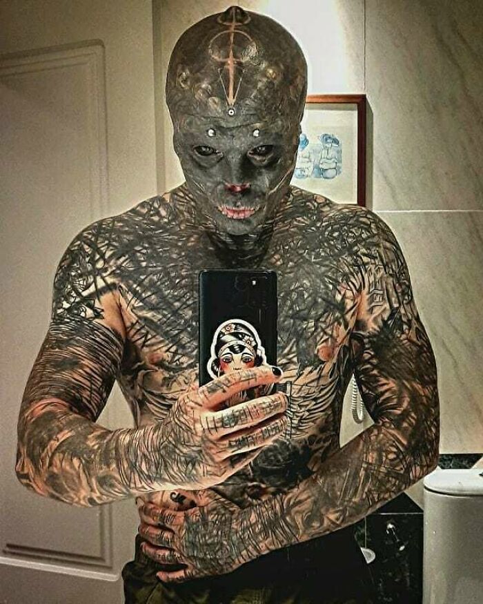 Heavily tattooed man with body modifications taking a selfie in a bathroom mirror. Heavily tattooed man with body modifications taking a selfie in a bathroom mirror.