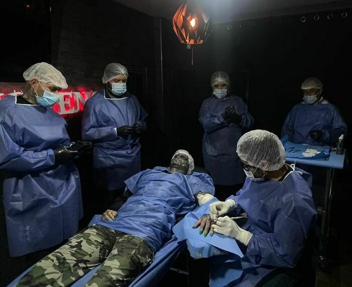 People in medical attire performing a procedure on the 'Black Alien' in a dimly lit room. People in medical attire performing a procedure on the 'Black Alien' in a dimly lit room.
