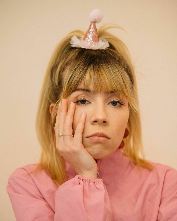Blonde woman in a pink top, resting her face on her hand against a neutral background. Blonde woman in a pink top, resting her face on her hand against a neutral background.