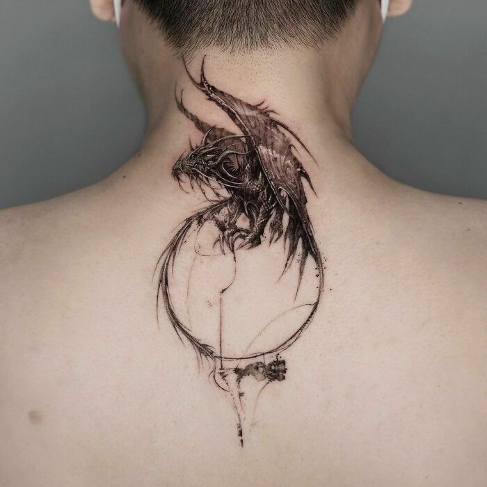 Gothic tattoo of a detailed dragon on a person's upper back, showcasing intricate artwork and dark themes.