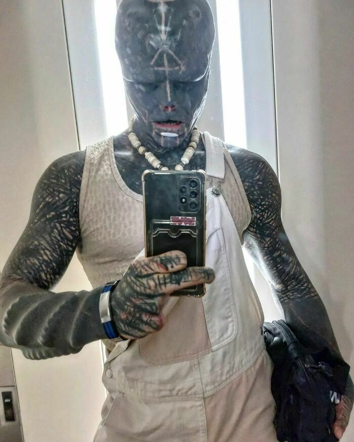 "Individual with tattoos and altered appearance takes a mirror selfie, highlighting unique personal expression. "Individual with tattoos and altered appearance takes a mirror selfie, highlighting unique personal expression.