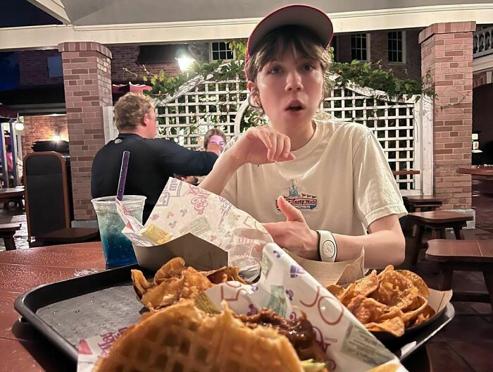 Person in a casual setting wearing a cap, with food on the table, discussing a story about her mother showering with her. Person in a casual setting wearing a cap, with food on the table, discussing a story about her mother showering with her.