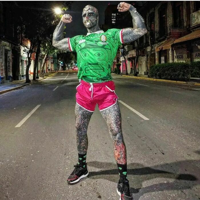 "Black Alien" standing in a street, flexing muscles in green jersey and pink shorts at night. "Black Alien" standing in a street, flexing muscles in green jersey and pink shorts at night.