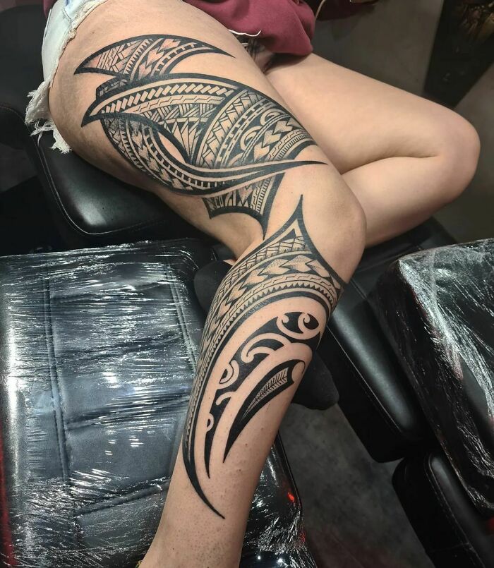 Person with detailed tribal tattoo design on their thigh and leg, showcasing bold black geometric patterns.