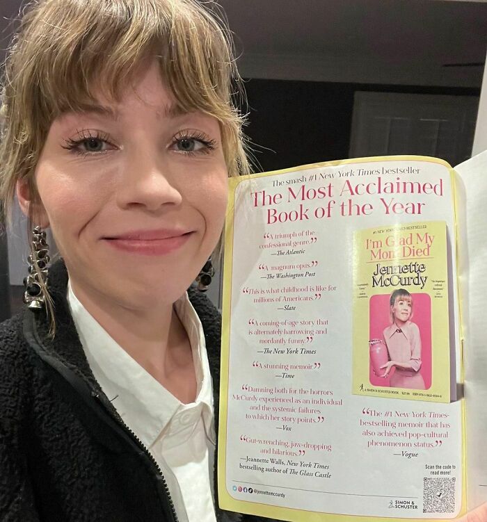 Jennette McCurdy smiling, holding open her acclaimed book "I'm Glad My Mom Died" featuring positive reviews. Jennette McCurdy smiling, holding open her acclaimed book "I'm Glad My Mom Died" featuring positive reviews.