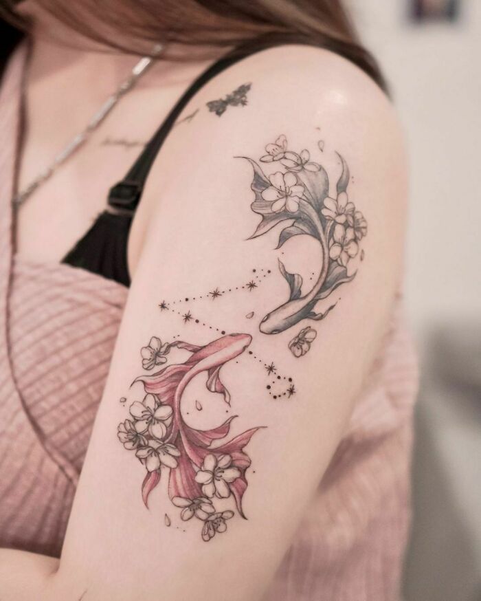 Zodiac tattoo of two fish intertwined with floral designs on an upper arm.