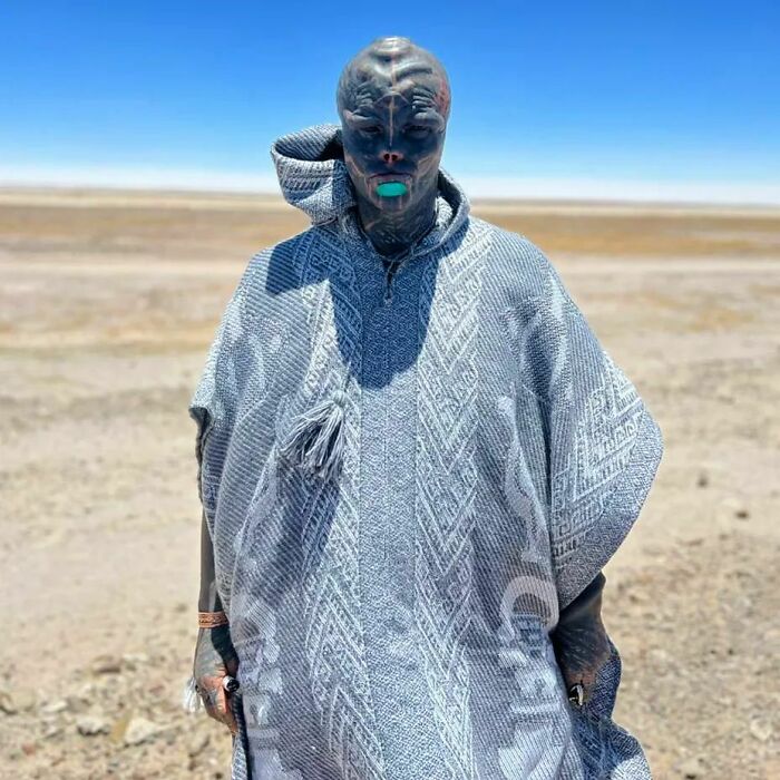 Person known as 'Black Alien' in a gray poncho standing in a desert landscape. Person known as 'Black Alien' in a gray poncho standing in a desert landscape.