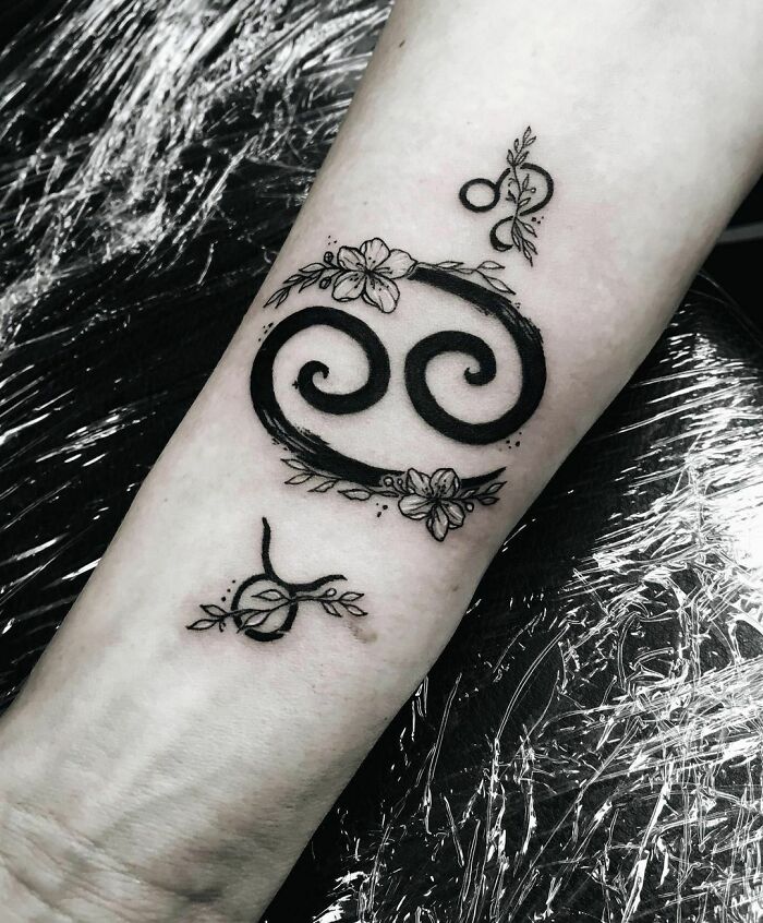 Zodiac tattoo design on forearm with intricate floral accents and swirling symbols.