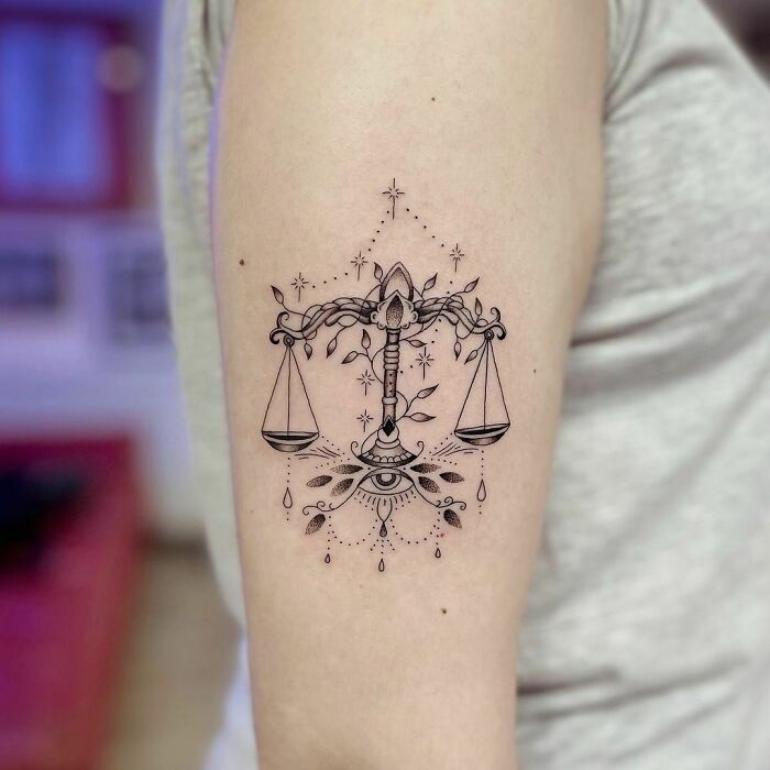 Ornate Libra zodiac tattoo on arm, featuring scales and decorative elements.