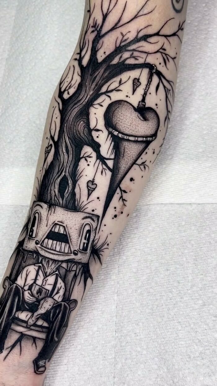 Gothic tattoo of a tree with hanging heart and a figure sitting, showcasing intricate line work on the forearm.