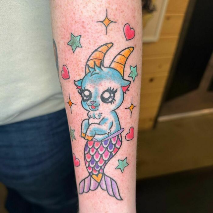 Colorful zodiac tattoo featuring a cute mermaid goat with stars and hearts on a person's forearm.