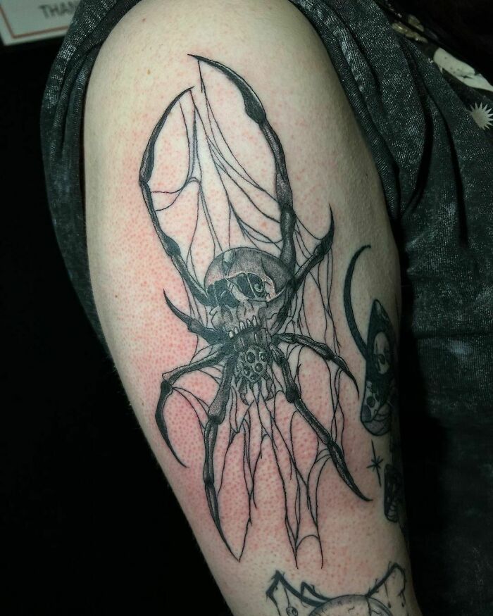 Intricate gothic tattoo of a winged skull and spider on an arm.