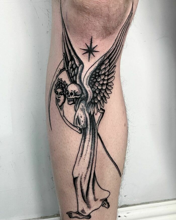 Gothic tattoo featuring a winged skeleton holding a mask, inked on a person's calf.