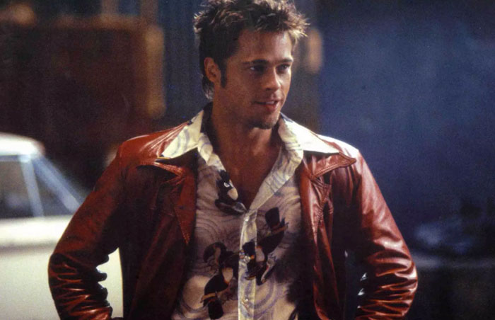 Young actor in a patterned shirt and brown jacket, drawing attention to age with a confident expression. Young actor in a patterned shirt and brown jacket, drawing attention to age with a confident expression.