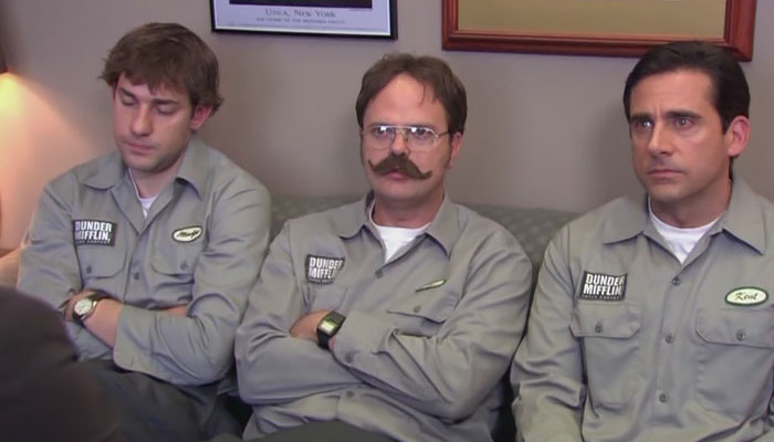 Jim Halpert, Dwight Schrute, Michael Scott all wearing dunder mifflin uniforms while sitting on a couch