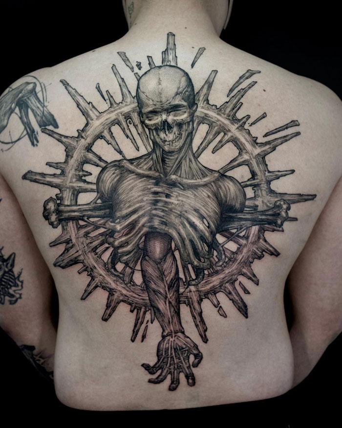 Gothic tattoo featuring a skeletal figure with detailed anatomy and circular design on a person's back.