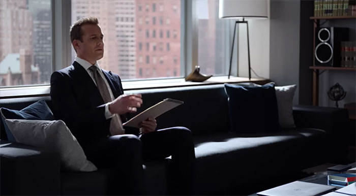 Harvey Specter sitting on sofa and reading from paper