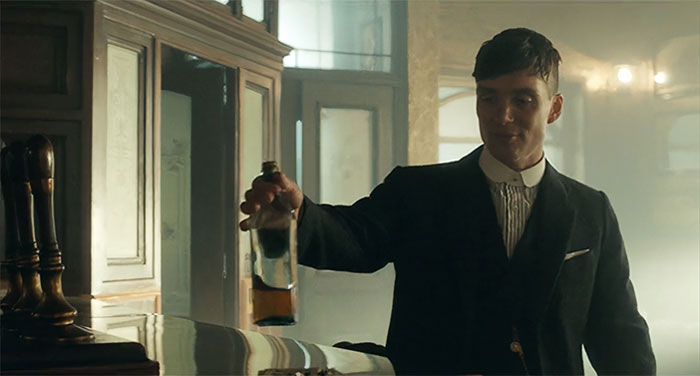 Tommy Shelby holding a bottle of whiskey
