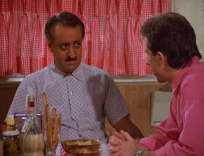 Babu Bhatt wearing a white shirt in a Seinfeld scene, illustrating funny Seinfeld quotes about everyday life.