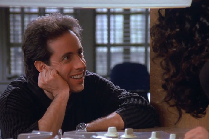 Jerry wearing a black sweater, smiling and engaged in conversation, illustrating funniest Seinfeld quotes about everyday life.