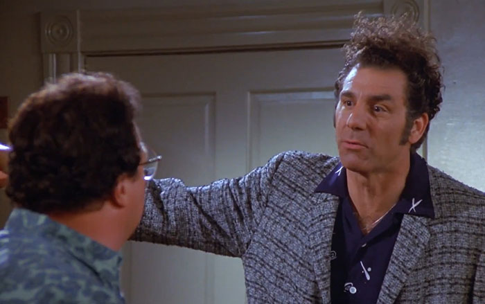 Cosmo Kramer in a gray suit and purple shirt, captured in a classic Seinfeld moment featuring funniest Seinfeld quotes.