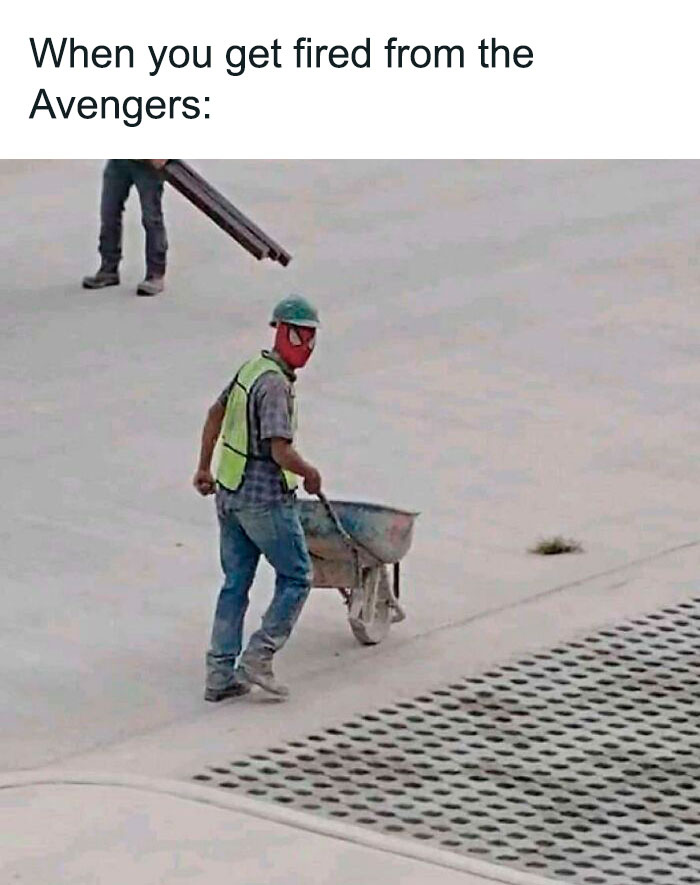 Construction worker wearing a Spiderman mask pushing a wheelbarrow, humorously implying a career change from superhero duties.