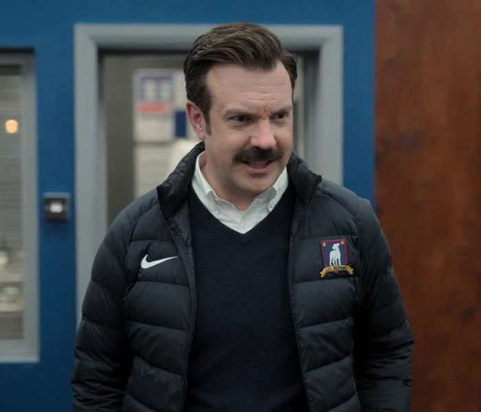 Ted Lasso wearing black sweater, white shirt and jacket