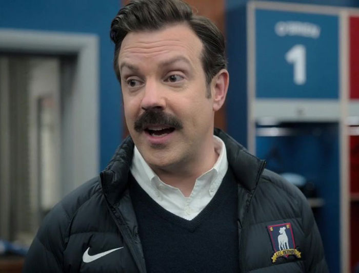 Ted Lasso wearing black sweater, white shirt and jacket