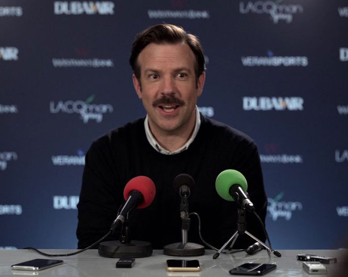 Ted Lasso wearing blue sweater and white shirt