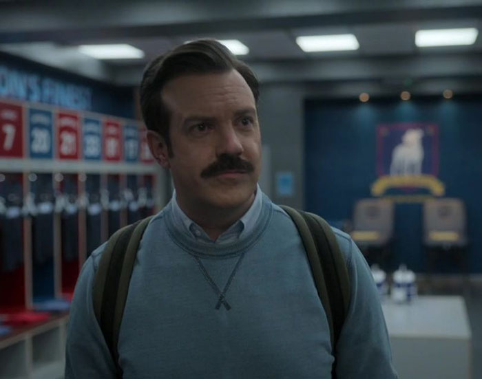 Ted Lasso wearing gray sweater and white shirt