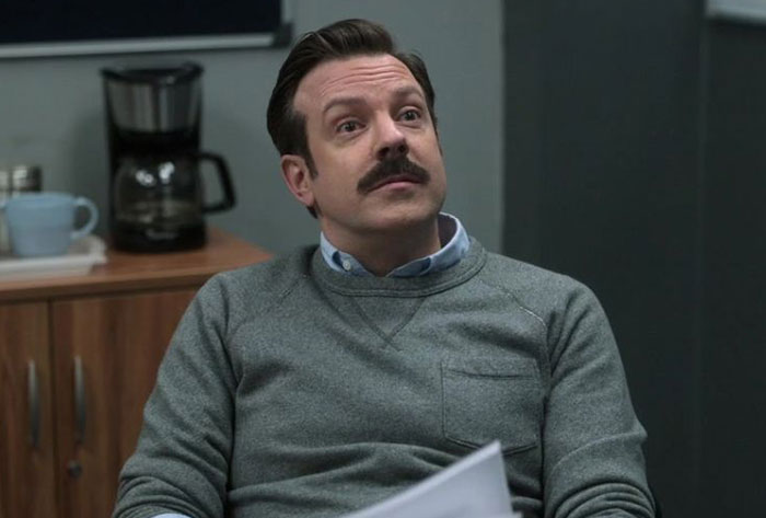Ted Lasso wearing gray sweater and blue shirt