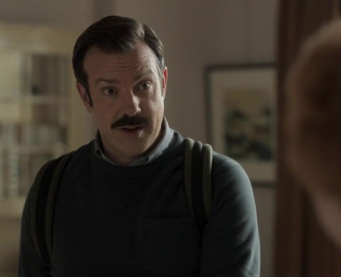 Ted Lasso wearing gray sweater and white shirt