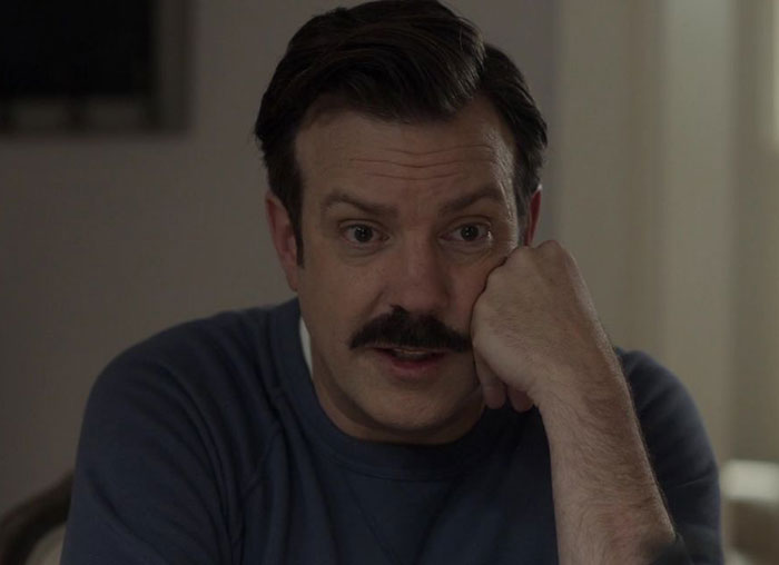 Ted Lasso wearing blue sweater and white shirt