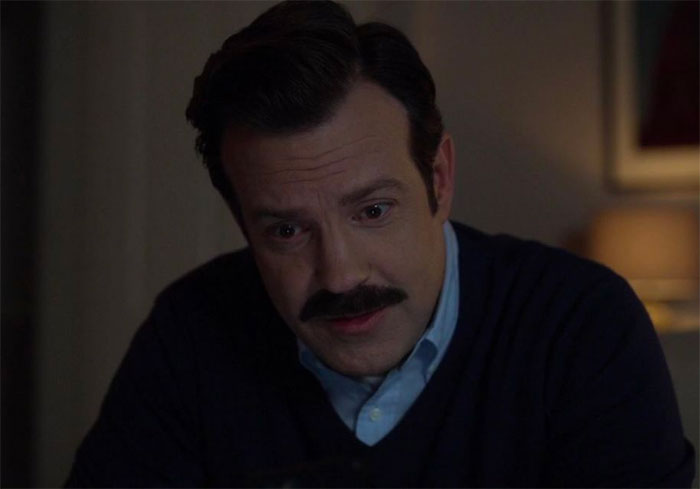 Ted Lasso wearing blue sweater and blue shirt