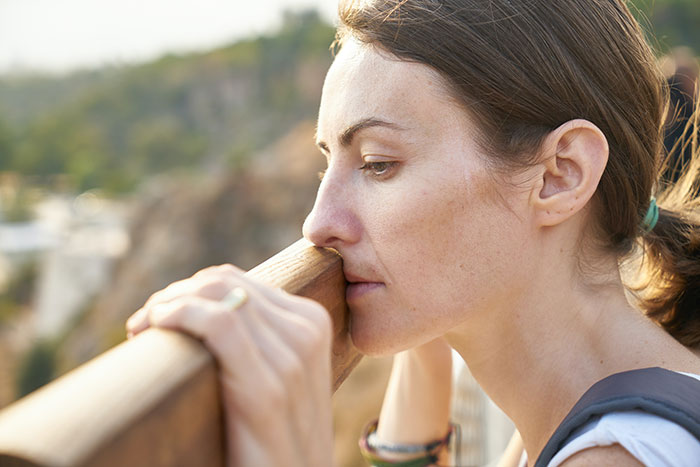 Mom looking distressed and reflective while leaning on a wooden railing outdoors, showing signs of emotional struggle. Mom looking distressed and reflective while leaning on a wooden railing outdoors, showing signs of emotional struggle.