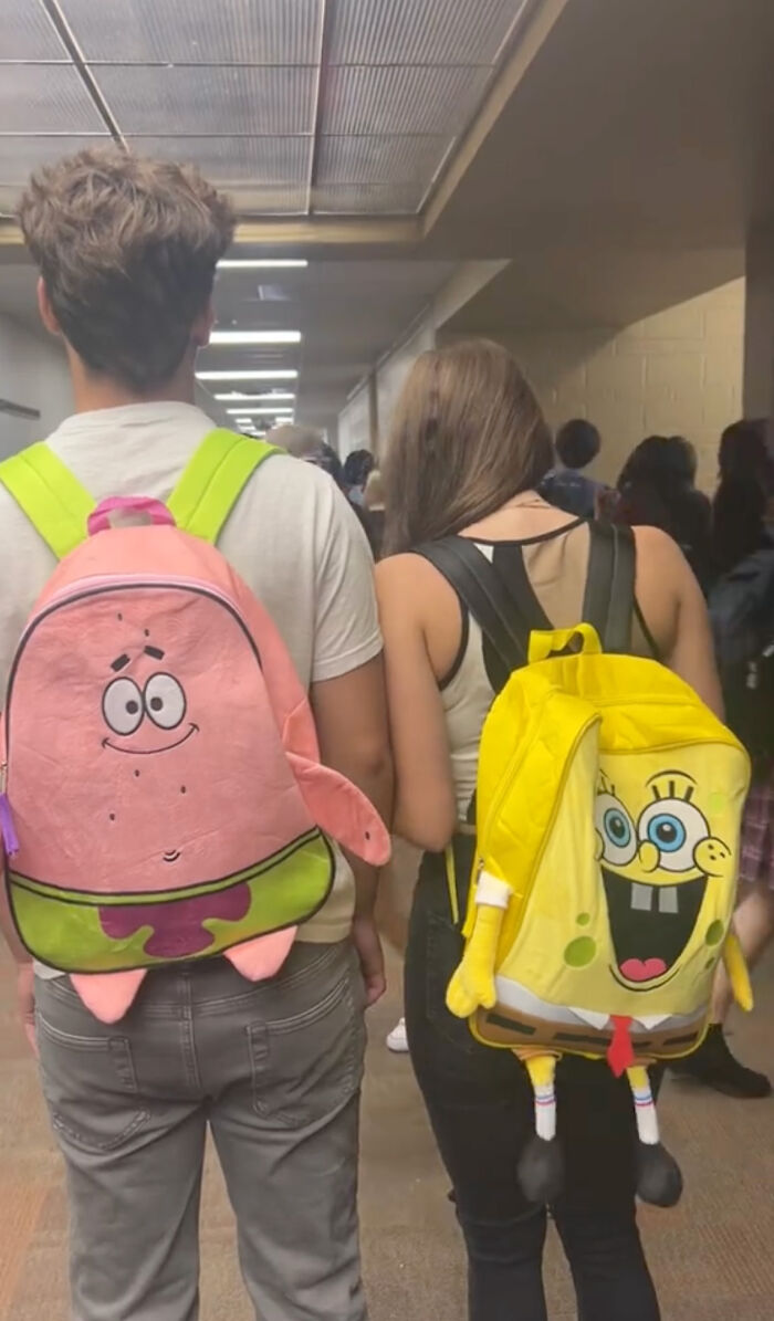 High school seniors wearing cartoon-themed kindergarten backpacks in a school hallway. High school seniors wearing cartoon-themed kindergarten backpacks in a school hallway.