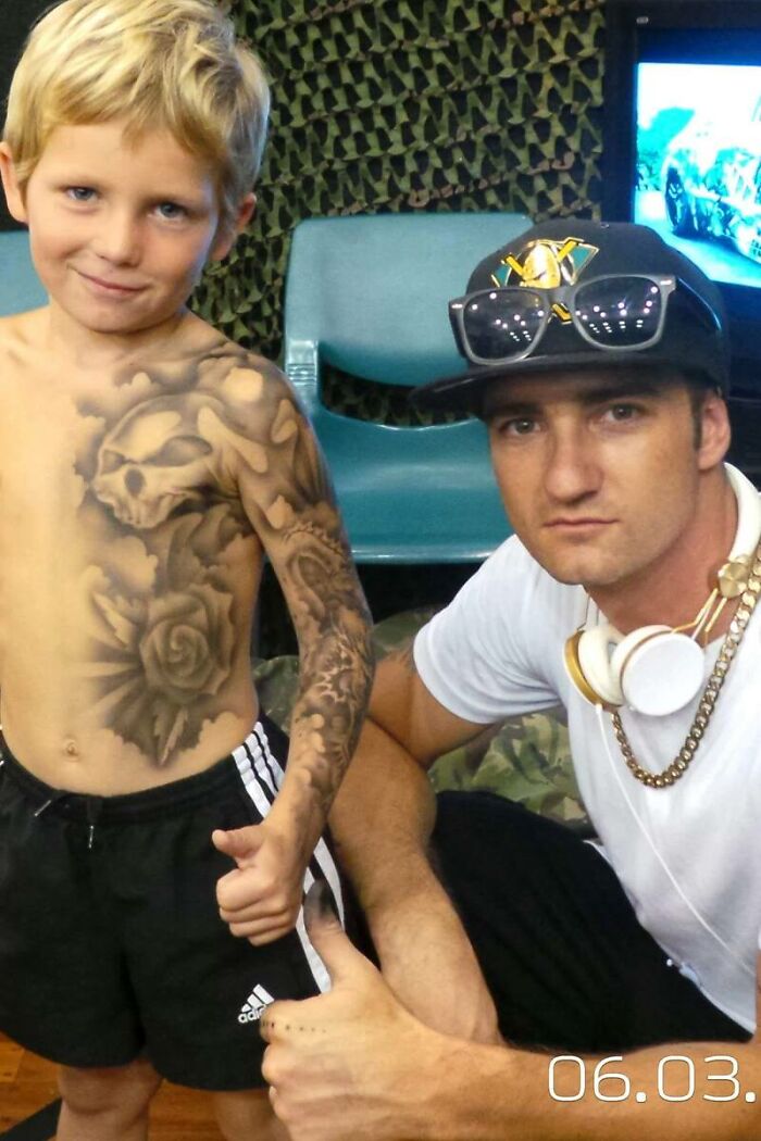 Artist with hospitalized kid showing spray-on tattoo, both giving thumbs up.