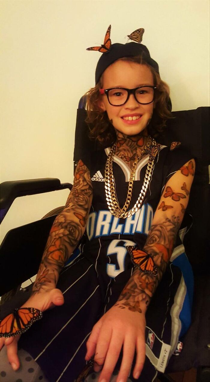 Smiling child with spray-on tattoos and butterfly designs, wearing sports jersey and glasses.