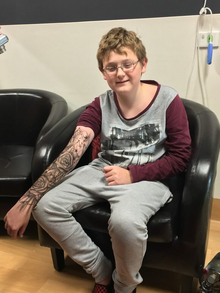 Hospitalized child with spray-on tattoo art, sitting on a chair with a smiling expression and detailed arm design.