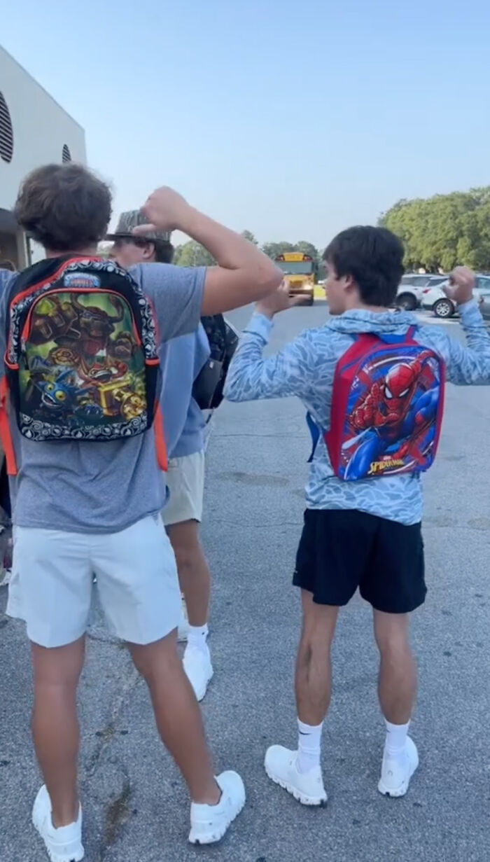High school seniors wearing colorful kindergarten backpacks, flexing playfully outside school. High school seniors wearing colorful kindergarten backpacks, flexing playfully outside school.