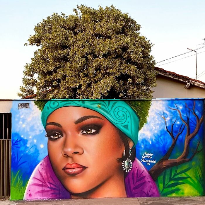 Street Artist Continues To Paint Portraits On Walls Next To Trees That Double As Hair
