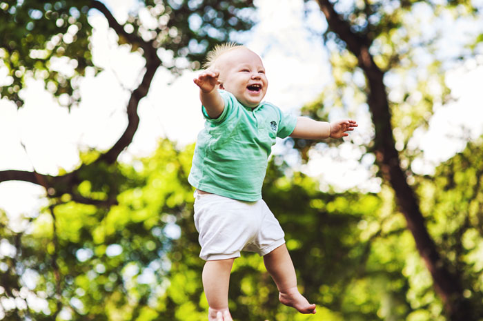 Happy toddler boy jumping outdoors in a green shirt and white shorts, related to woman speaking Polish to their kid. Happy toddler boy jumping outdoors in a green shirt and white shorts, related to woman speaking Polish to their kid.